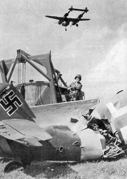 USAAF engineer clearing out a captured airstrip, somewhere in Europe, circa 1945; note P-38 Lightning aircraft flying overhead with landing gear down