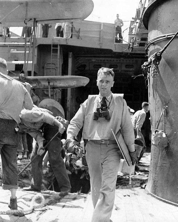 US Navy pilot Lt Wilson R. Bartlett of cruiser Chester returning from observation flight to Taroa, Marshall Islands, 1 Feb 1942; note bomb damage in background and wingtips of his SOC Seagull aircraft