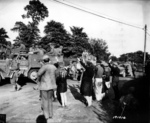 US Army troops drive by the people of Montebourg, Normandy, France, June 1944.  Note M2 Half-Track “Dirty Gertie” and M4 Sherman Duplex-Drive tank with soldiers sitting on the folded skirt frame.