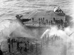 Crews aboard USS Enterprise controlling fires from a Japanese bomb that blew the forward elevator completely out of the ship, shearing off the tail of an F6F Hellcat as it exited, off Kyushu, Japan, 14 May 1945.