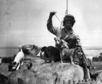 US Marine Private Bruce Rutherford cleaning his Thompson submachine gun while playing with puppies Nanci, Shoto, Sake, Zero, Banzai, and Okinawa on Okinawa, Japan, 1 Jun 1945