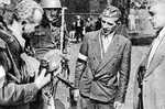 Polish resistance fighter Captain Cyprian Odorkiewicz inspecting a captured German Army cap held by Wacław Jastrzębowski, Okólnik gardens, Warsaw, Poland, 14 Aug 1944; note captured MP 40 submachine gun