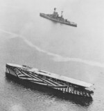 HMS Argus in dazzle camouflage in a British harbor, circa late 1918; note R-class battleship in background