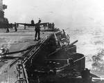 Damage to Lexington port side number six 5-in gun by dive bomb, Battle of Coral Sea, 8 May 1942, photo 2 of 2; note TBD-1 Devastator bomber on deck and F4F-3 Wildcat fighter approaching to land