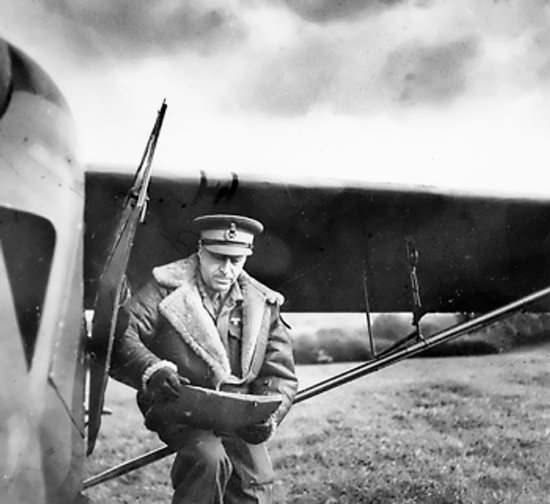 Lieutenant General Crerar looking at a map while sitting on the wing strut of a light observation plane, circa 1944