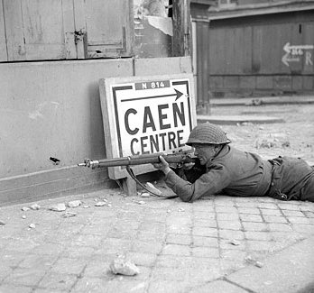 A British soldier with Lee-Enfield No. 4 rifle on a street in Caen, France, 9 Jul 1944