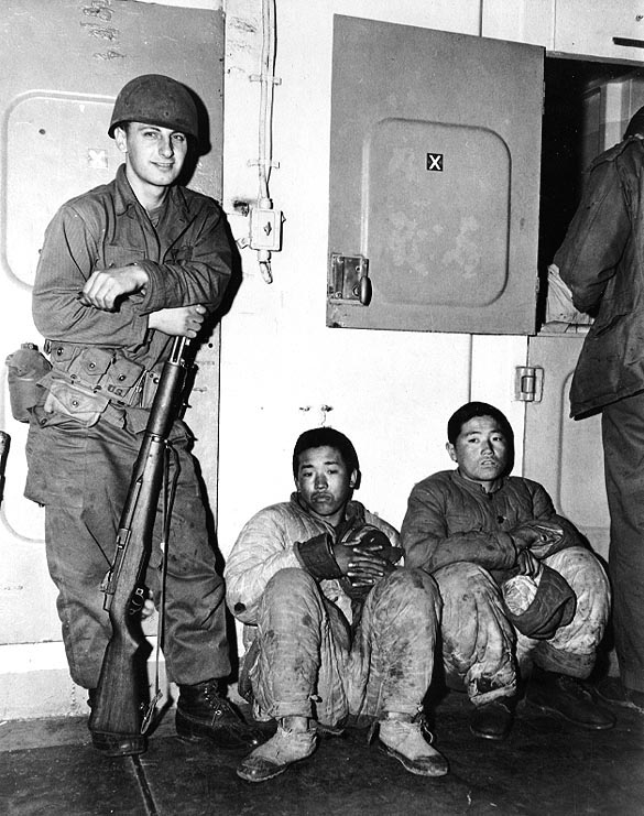 US Marines guarding 2 North Korean prisoners aboard a transport ship which was probably traveling from Hungnam to Busan, Korea, late Dec 1950; note M1 Garand rifle with safety at 'off' position